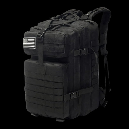 A black tactical military backpack with multiple zippered compartments, MOLLE webbing, compression straps, and a black-and-white American flag patch on the side, shown on a white background.